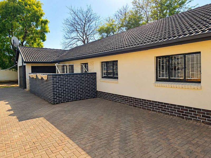 Rear exterior view of the property featuring a paved courtyard, brick boundary wall, and tiled roof with secure window bars.