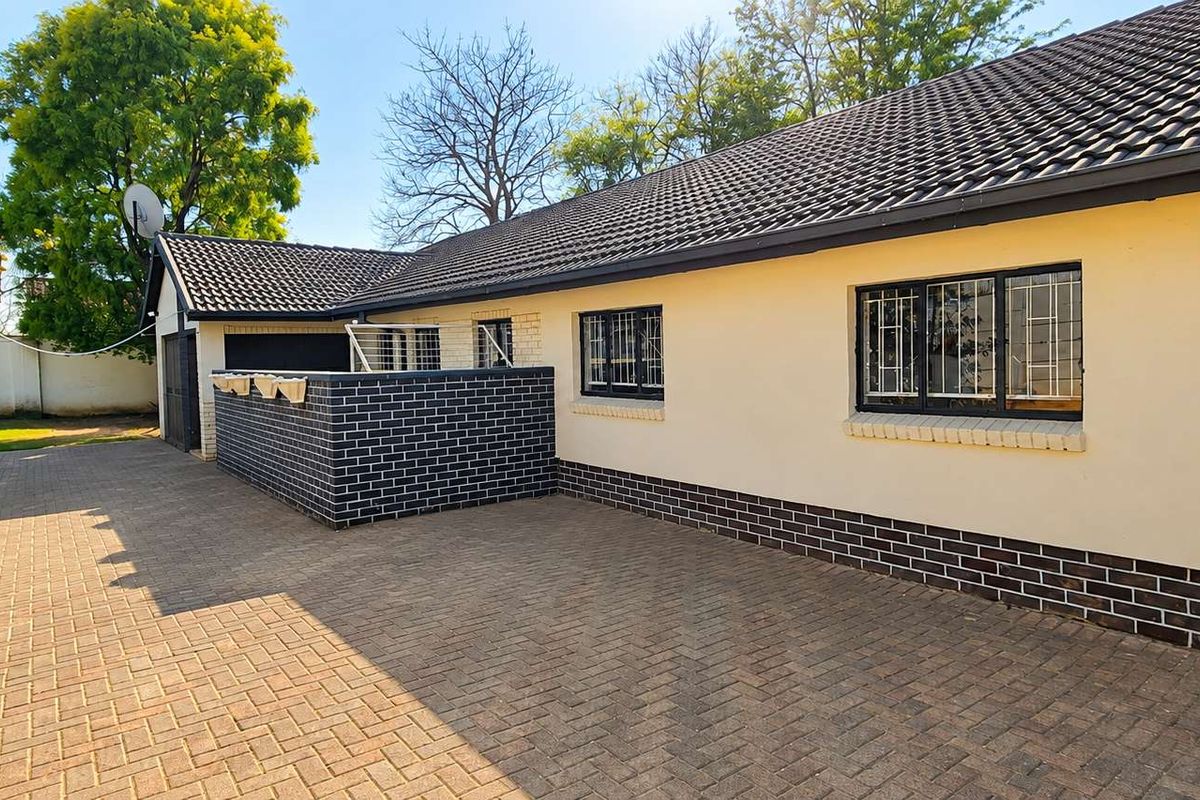 Rear exterior view of the property featuring a paved courtyard, brick boundary wall, and tiled roof with secure window bars.