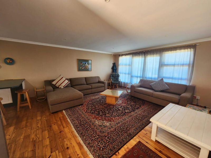 Spacious living room featuring warm hardwood flooring, cove molding, and large windows that provide ample natural light.