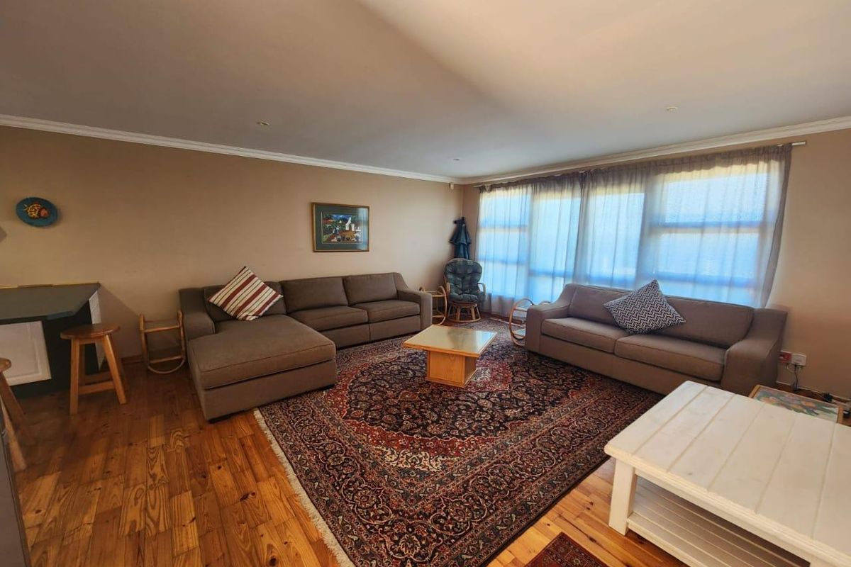 Spacious living room featuring warm hardwood flooring, cove molding, and large windows that provide ample natural light.