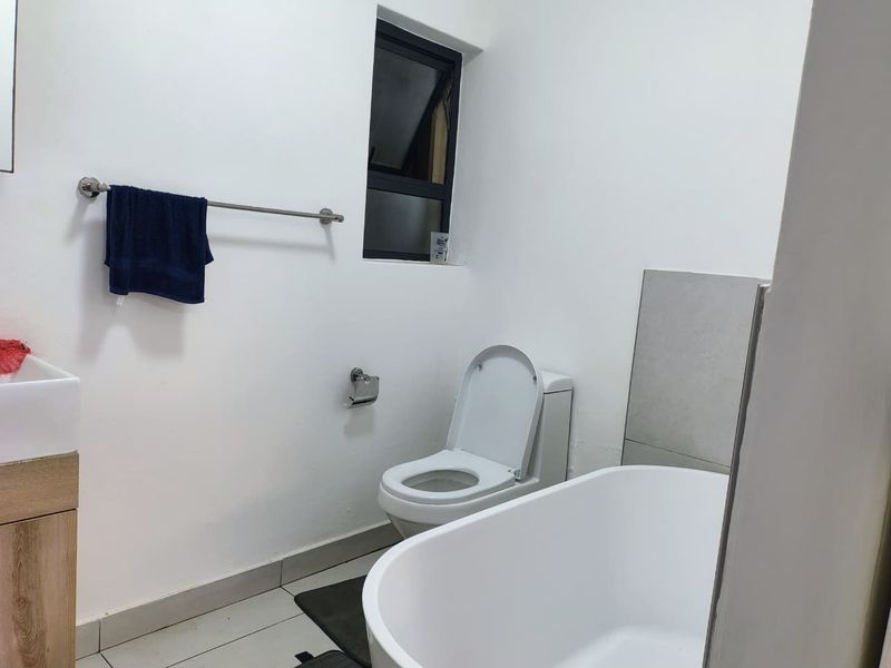 A clean, modern bathroom featuring a freestanding bathtub, a vanity with basin, and a toilet, finished with neutral wall paint and tiled flooring.