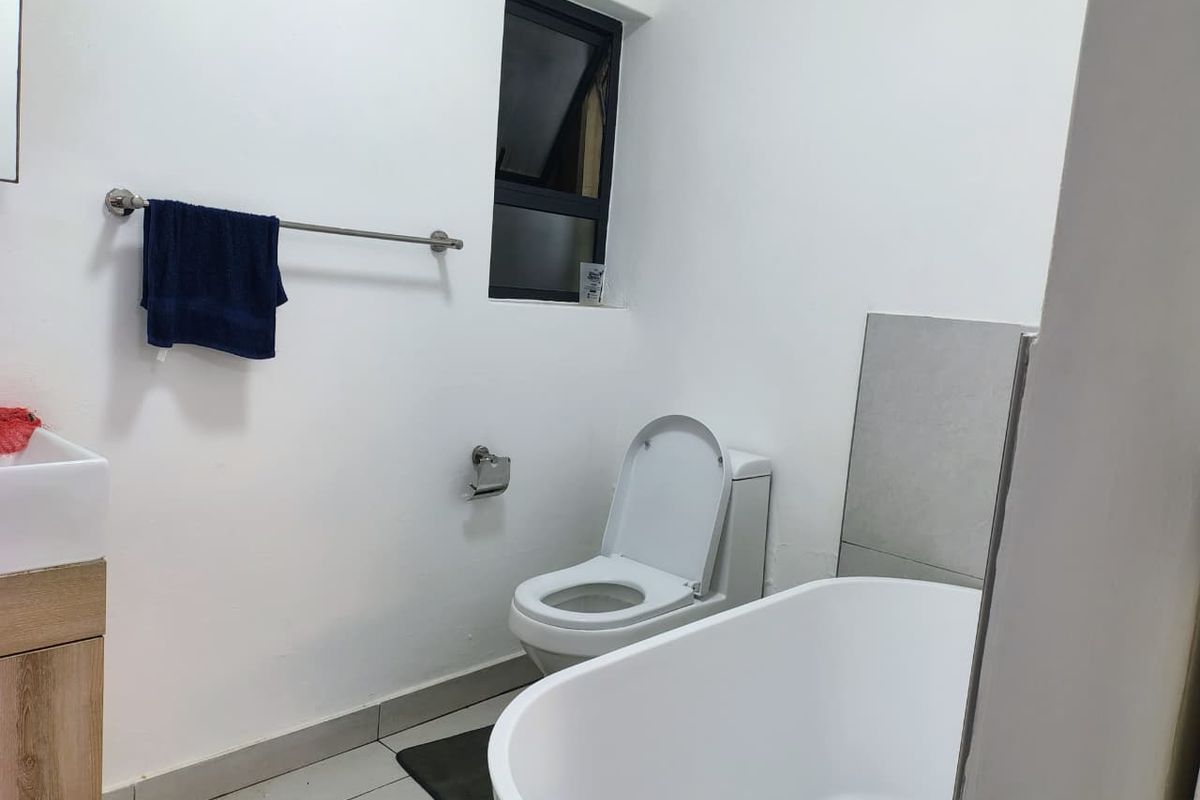 A clean, modern bathroom featuring a freestanding bathtub, a vanity with basin, and a toilet, finished with neutral wall paint and tiled flooring.