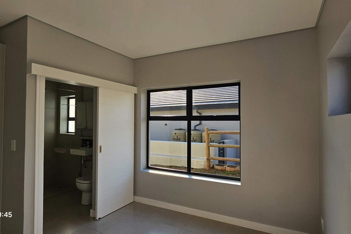 A modern, empty bedroom featuring neutral walls, tiled flooring, and a sliding door leading to an en-suite bathroom with contemporary finishes.