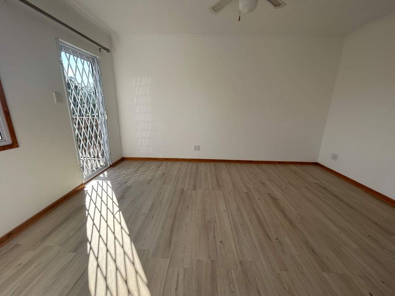 A bright, empty bedroom featuring modern laminate flooring, a ceiling fan, and a secure exterior door with a metal security gate.