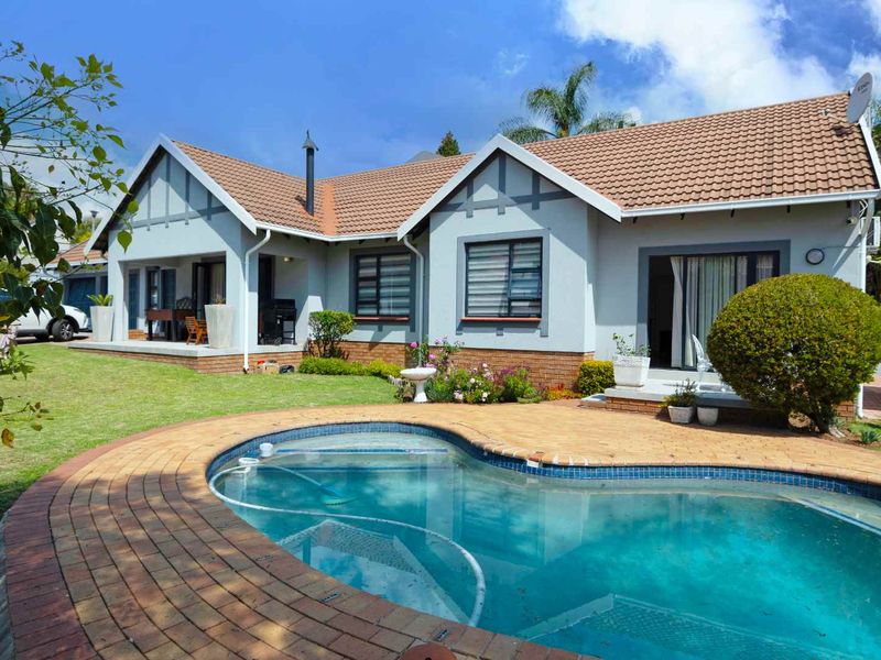 Rear view of the house featuring a swimming pool with brick paving, a covered patio area, and a well-maintained garden.