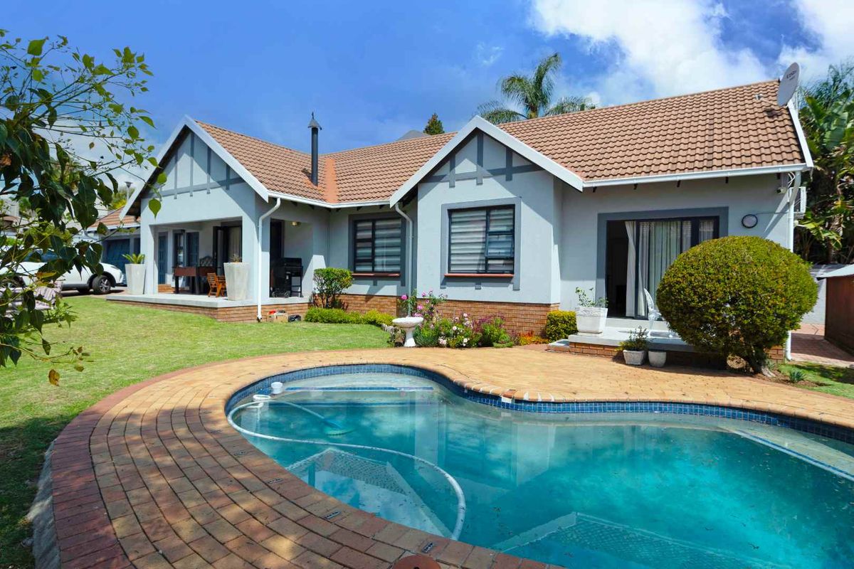 Rear view of the house featuring a swimming pool with brick paving, a covered patio area, and a well-maintained garden.