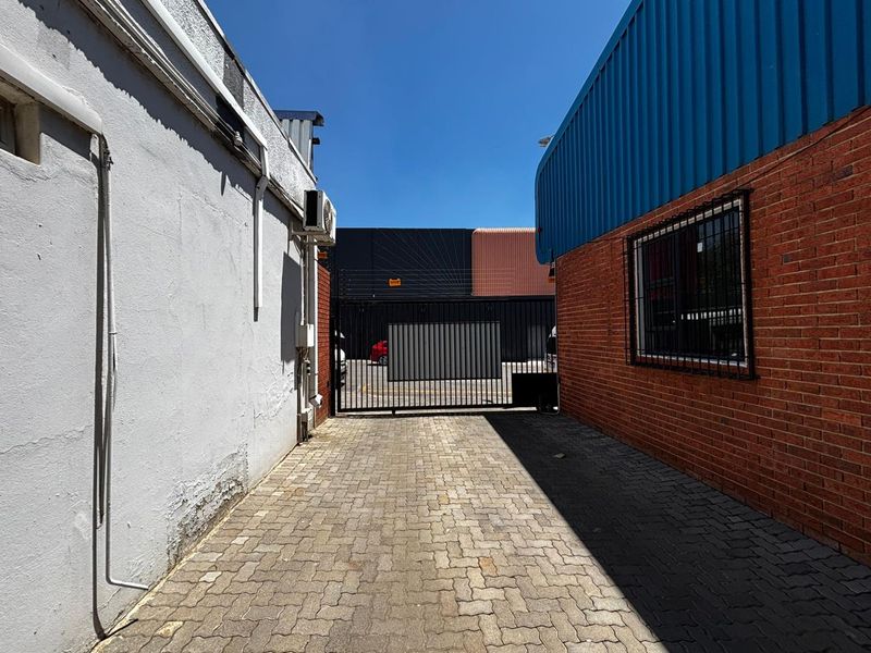 Rear exterior view of the business property featuring a paved driveway, secure metal gate, and brick and plaster wall finishes.
