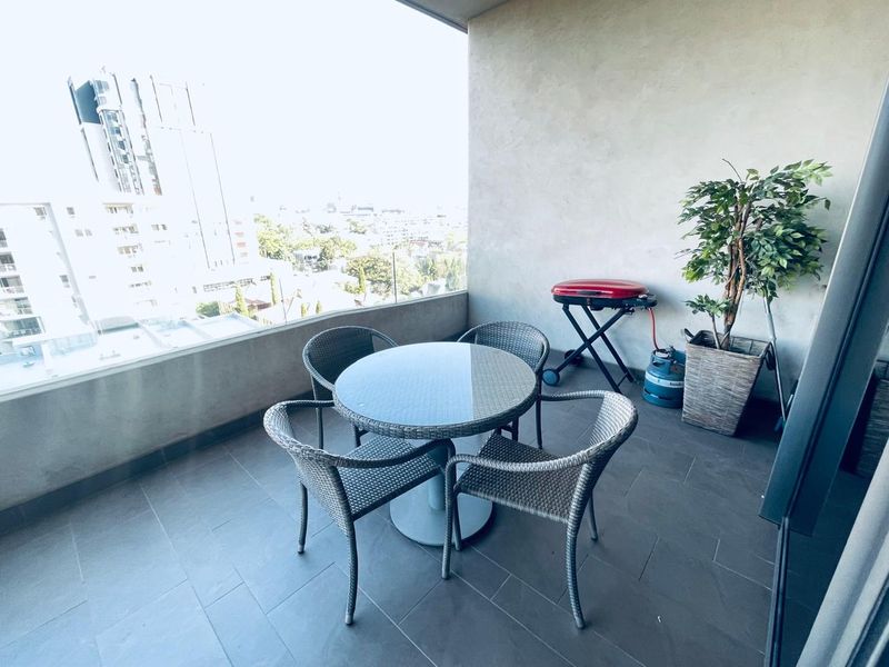 A covered balcony featuring tiled flooring and a glass balustrade, offering an elevated urban view.