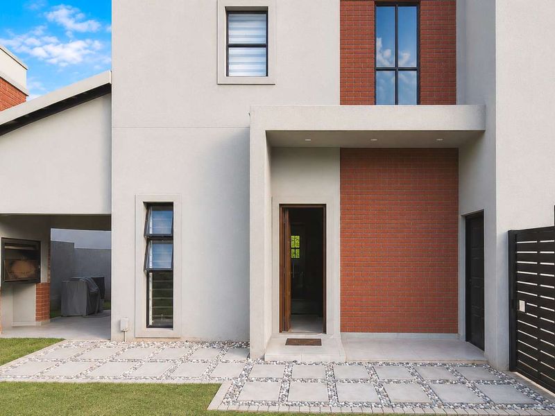 Modern rear exterior featuring a paved patio area, built-in braai, and a clean brick and plaster facade.