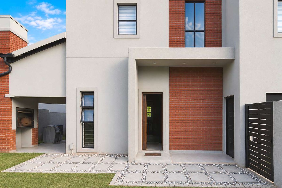 Modern rear exterior featuring a paved patio area, built-in braai, and a clean brick and plaster facade.