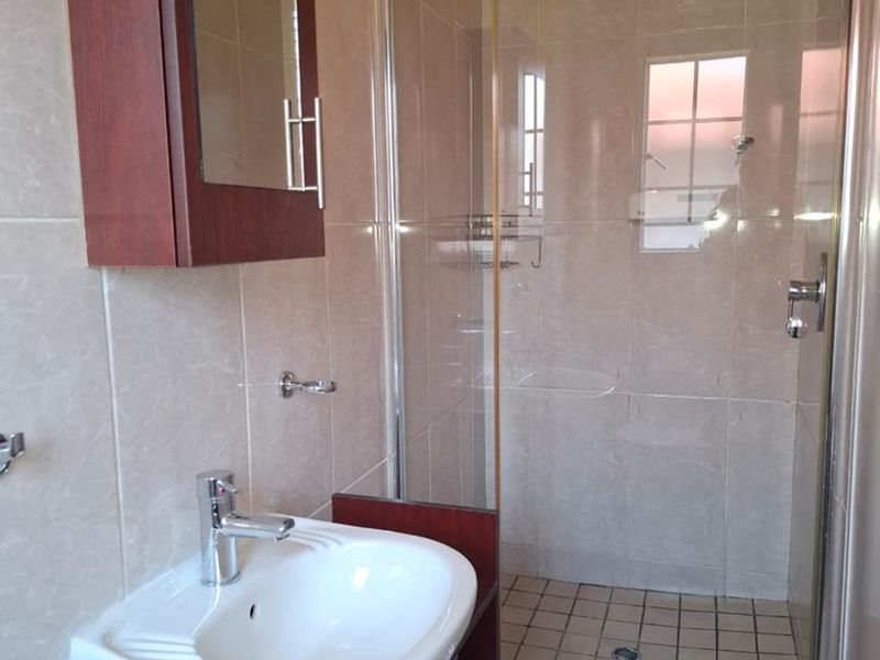 A functional bathroom featuring a glass-enclosed shower, wall-mounted vanity with basin, and neutral wall tiling.