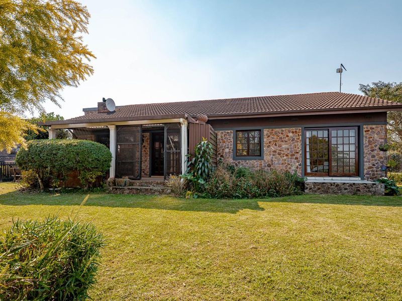 Rear view of the townhouse featuring stone cladding, a tiled roof, and a covered patio area overlooking a private garden.