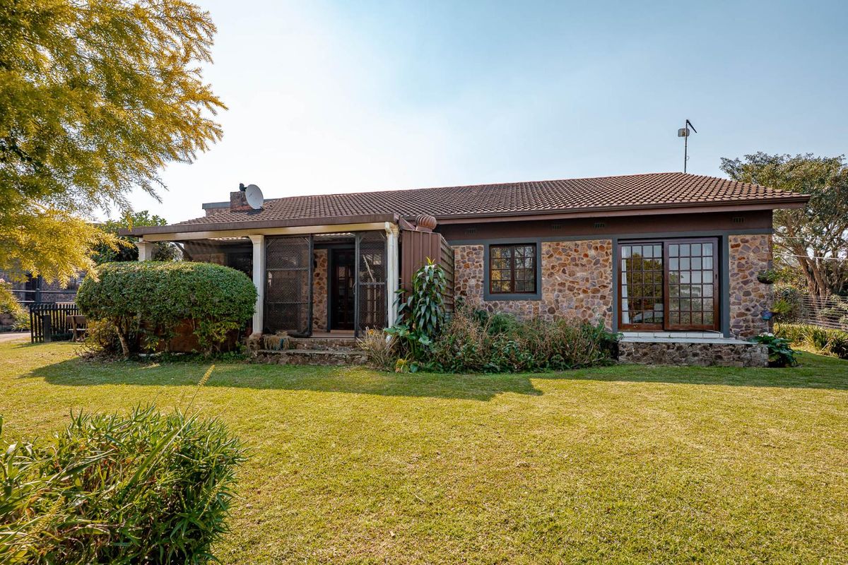 Rear view of the townhouse featuring stone cladding, a tiled roof, and a covered patio area overlooking a private garden.