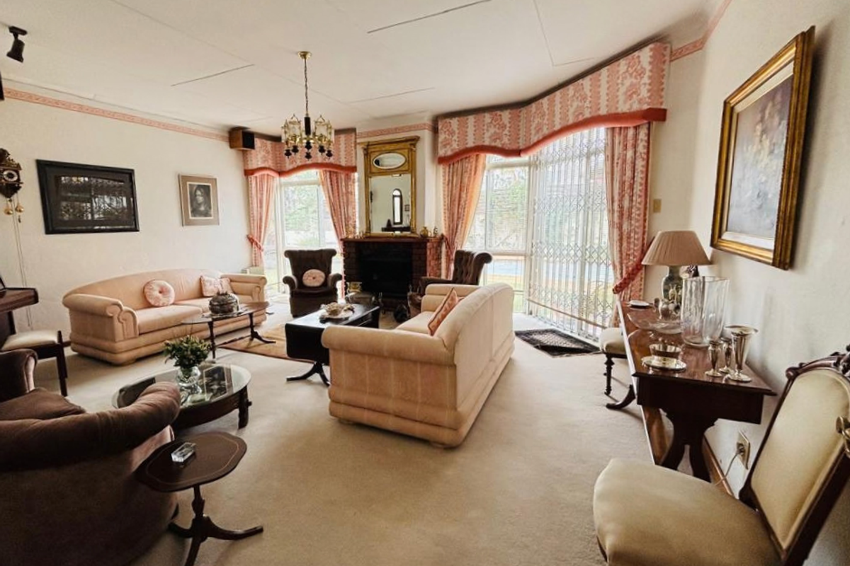Spacious living room featuring a traditional fireplace, bay window with security gate, and classic ceiling detailing, offering a comfortable and well-proportioned lounge area.