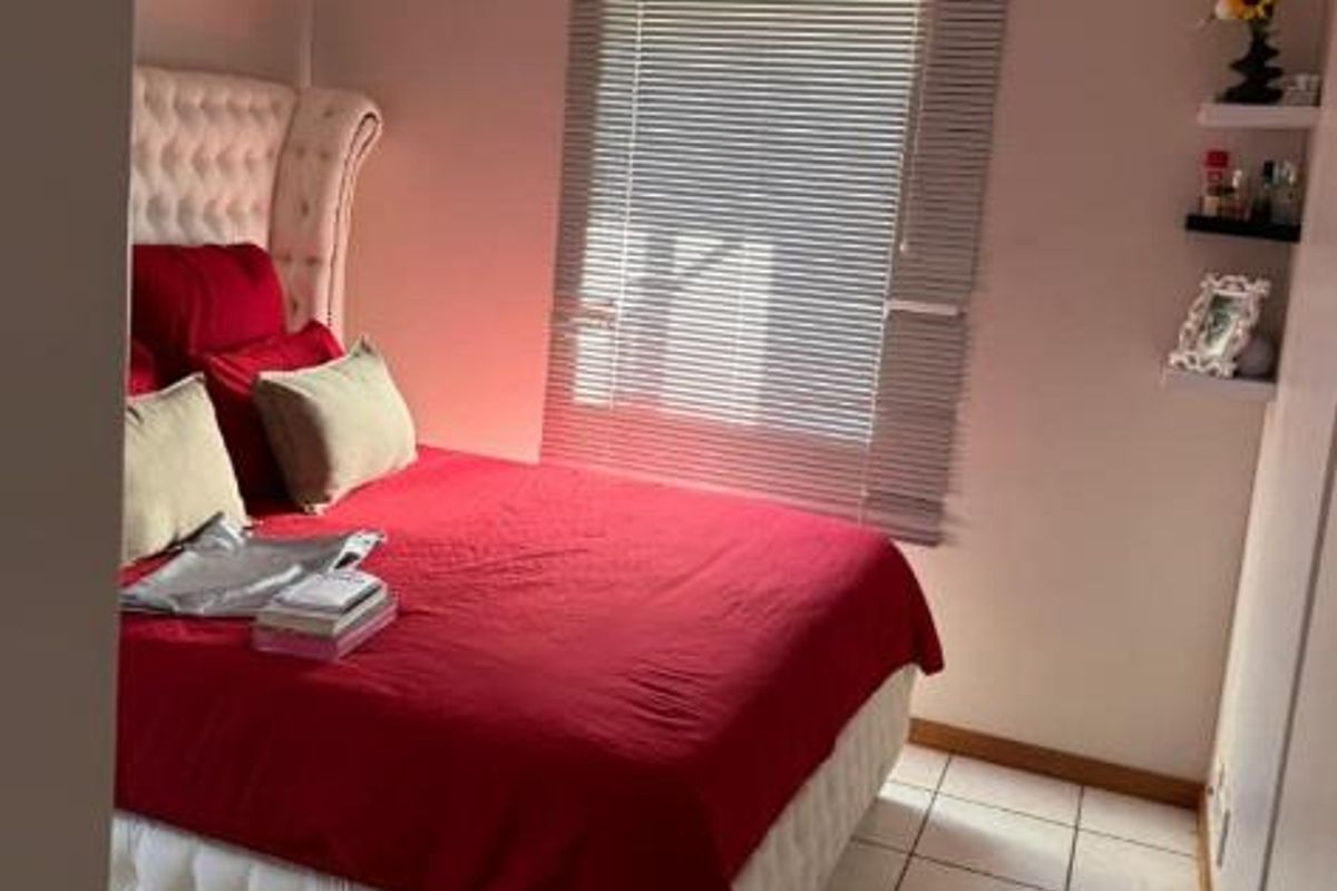 A compact bedroom featuring tiled flooring, a window with venetian blinds, and built-in floating wall shelves.