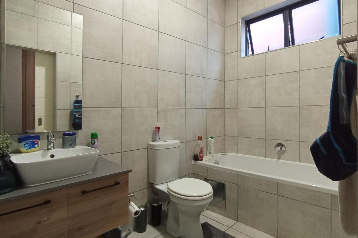 A modern bathroom featuring full-height wall tiling, a floating vanity with a vessel sink, a built-in bathtub, and a toilet.