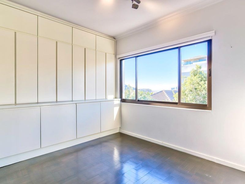 A bright, empty bedroom featuring extensive built-in cabinetry, dark hardwood flooring, and a large sliding window with an exterior view.