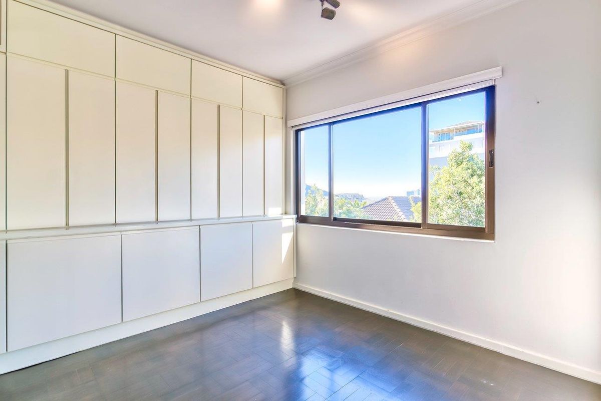 A bright, empty bedroom featuring extensive built-in cabinetry, dark hardwood flooring, and a large sliding window with an exterior view.