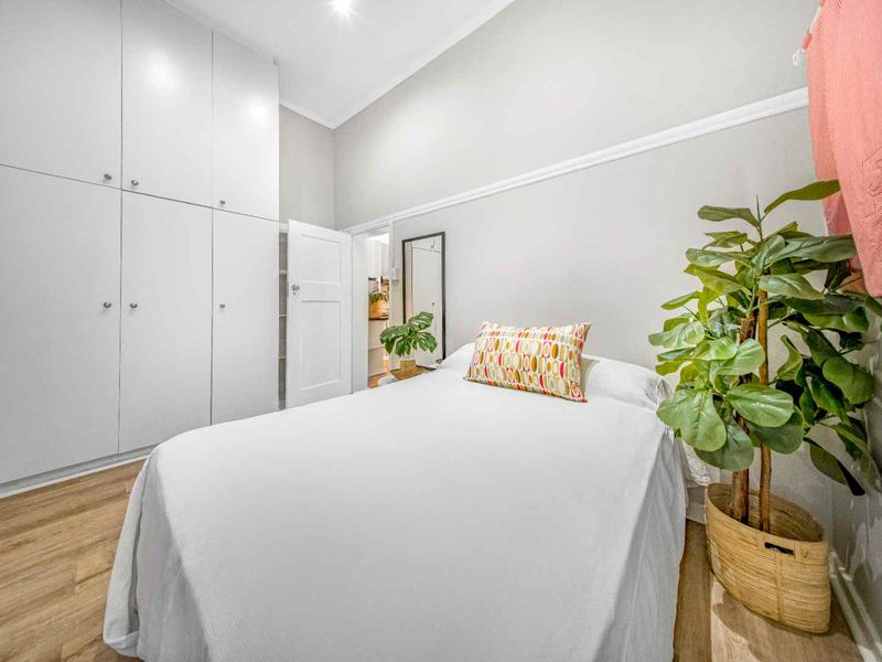 A well-maintained bedroom featuring light laminate flooring, neutral walls, and floor-to-ceiling built-in cupboards providing ample storage space.