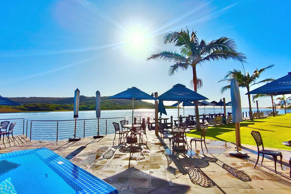 Outdoor pool area featuring stone paving, a metal balustrade, and a landscaped lawn overlooking a scenic waterfront.