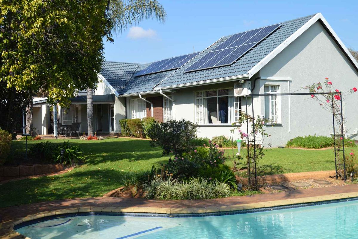 Rear view of the house featuring a well-maintained garden, swimming pool, and roof-mounted solar panels.