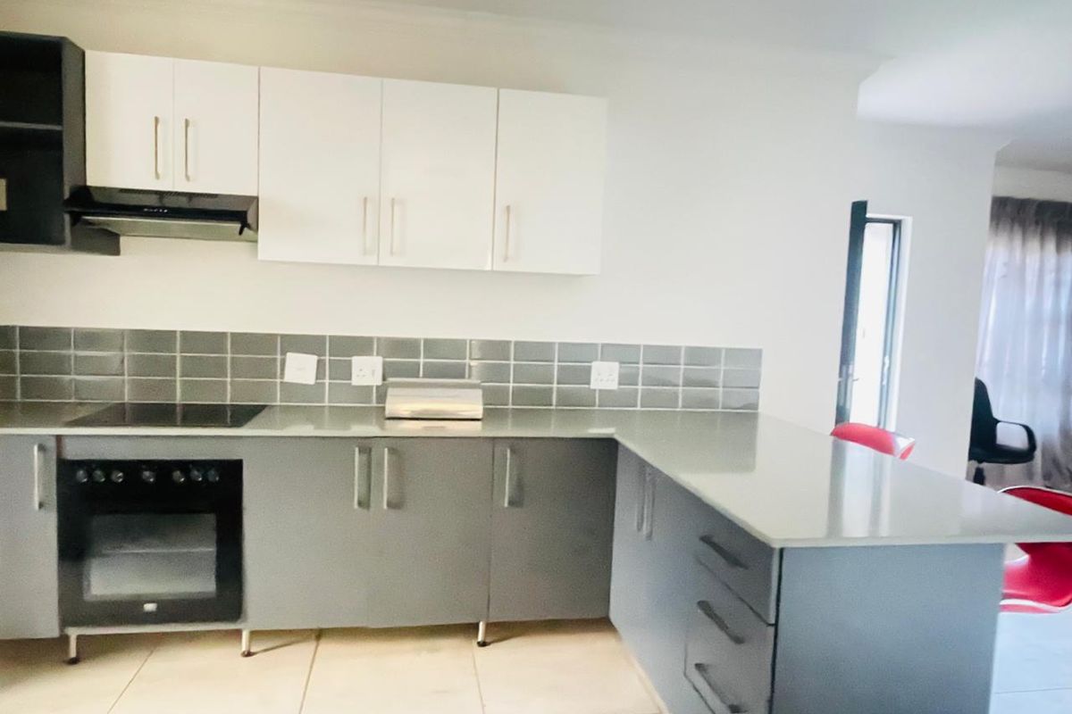 Modern kitchen featuring two-tone cabinetry, stone countertops, a built-in oven, electric hob, and a tiled backsplash, seamlessly integrated into an open-plan living space.
