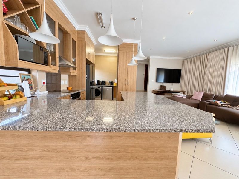 Spacious open-plan kitchen and living area featuring granite countertops, modern wood-finish cabinetry, integrated appliances, and a seamless flow into the adjacent living space.