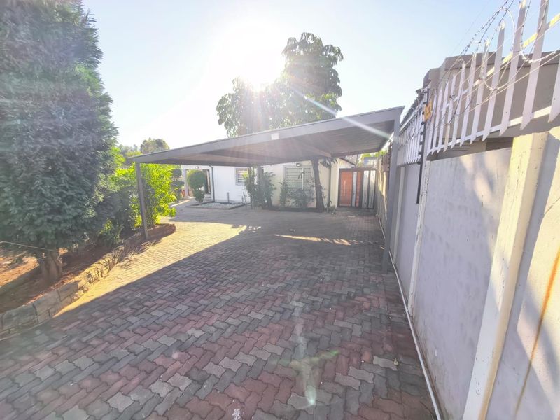 Front exterior view featuring a paved driveway, a covered carport, and a secure perimeter wall with electric fencing.