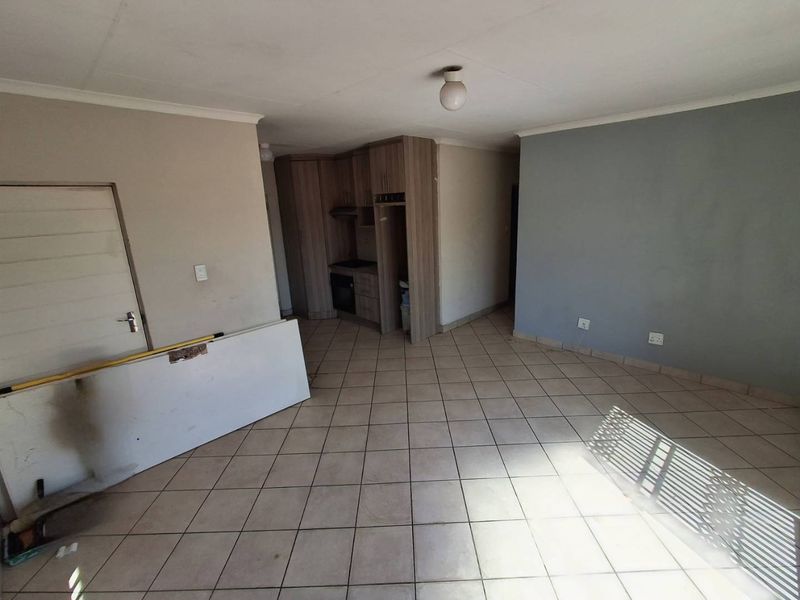An open-plan living and kitchen area featuring tiled flooring, built-in cabinetry, and an integrated oven, currently in a vacant state.