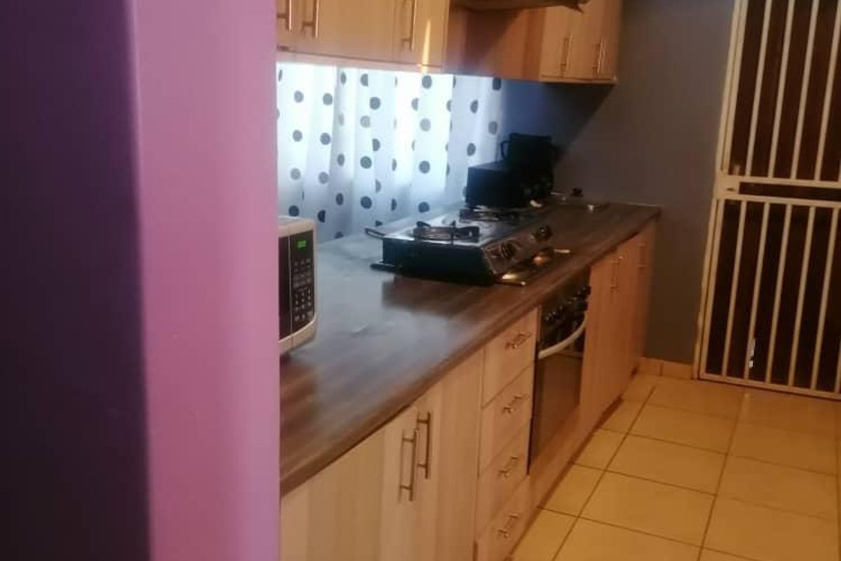 A functional kitchen featuring light wood-finish cabinetry, a built-in oven, gas hob, and extractor fan, with tiled flooring and a security gate.