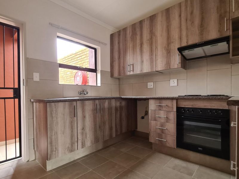 Modern kitchen featuring wood-look cabinetry, built-in oven with extractor fan, tiled backsplash, and direct access to an outdoor area via a security gate.