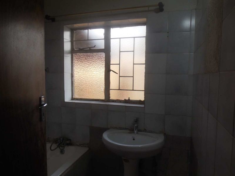 A dated bathroom featuring a pedestal basin, built-in bathtub, and tiled walls, requiring modernization and maintenance of fixtures.