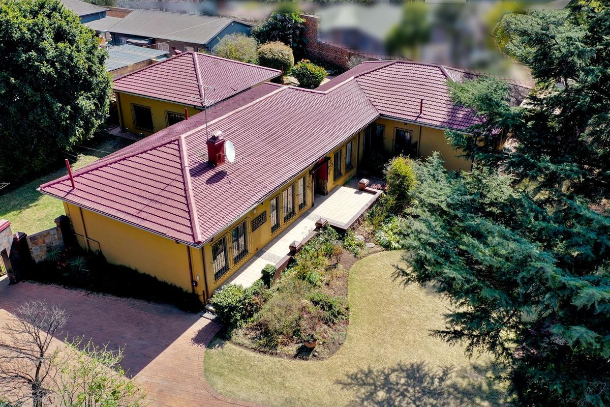 Aerial view of a residential property featuring a tiled roof, brick paved driveway, and established garden surroundings.