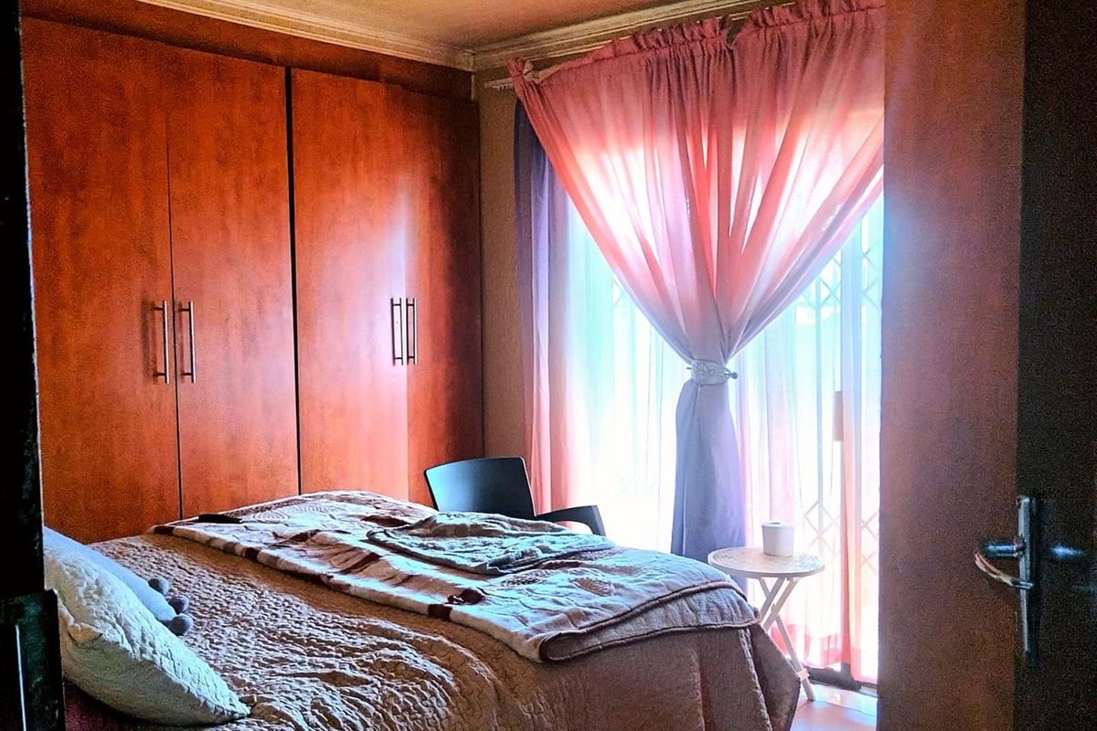 A bedroom featuring built-in wooden cupboards, tiled flooring, and a sliding door with a security gate providing access to the exterior.