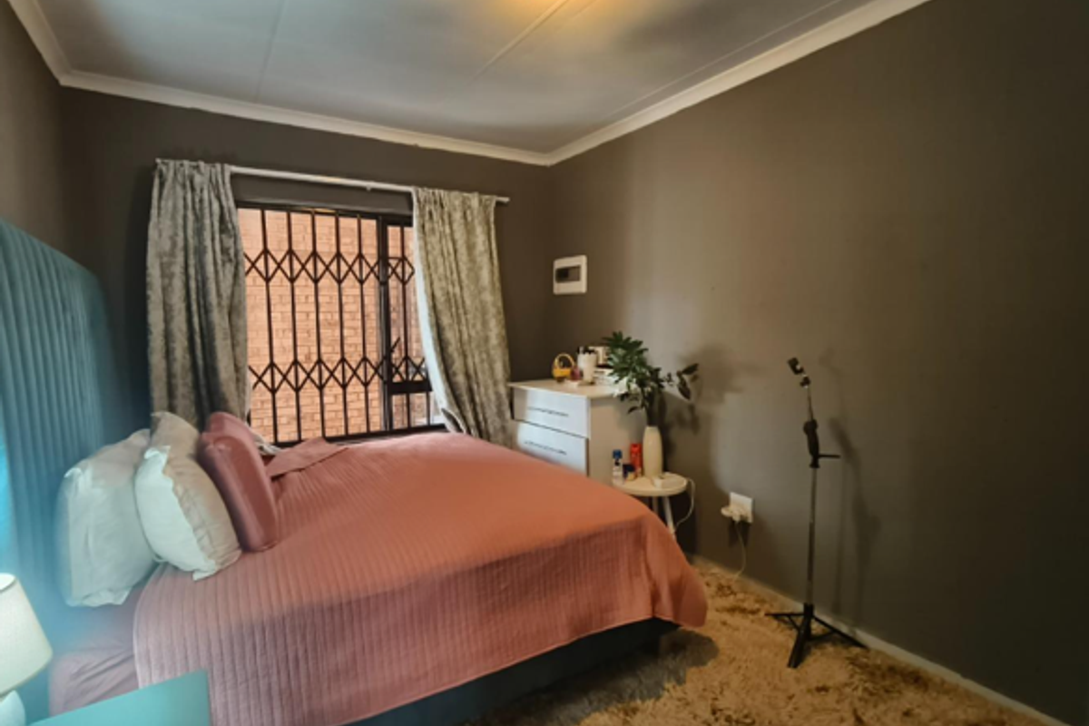 A bedroom featuring dark painted walls, a security gate on the window, and a ceiling light fixture.