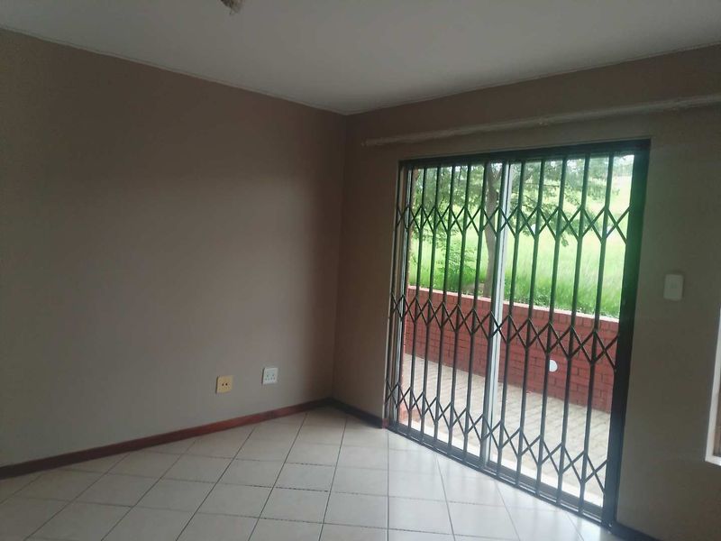 An empty living room featuring tiled flooring and a sliding glass door with a security gate, providing access to an outdoor patio area.