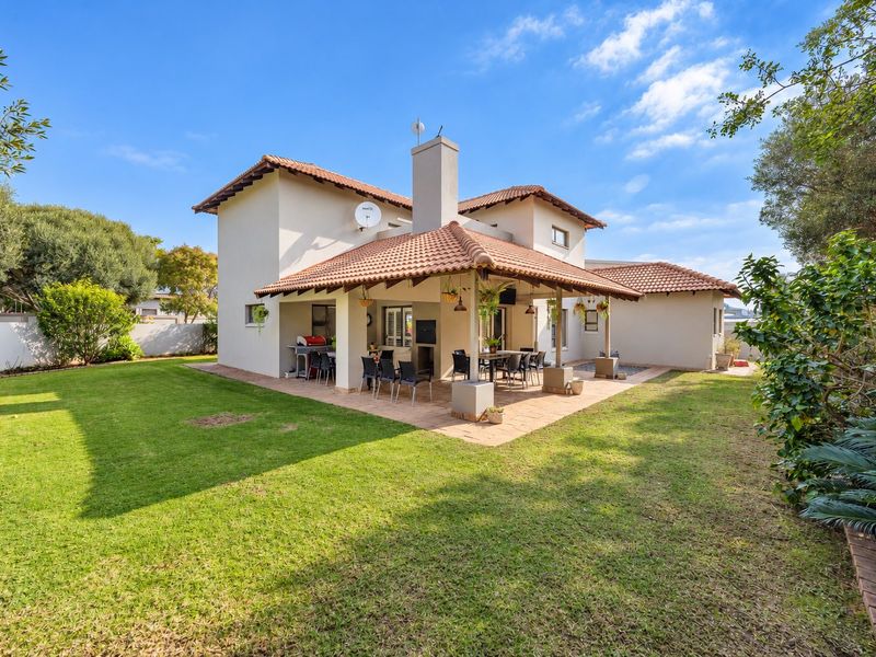 Rear view of the house featuring a spacious covered patio with a built-in braai, overlooking a well-maintained garden and lawn area.