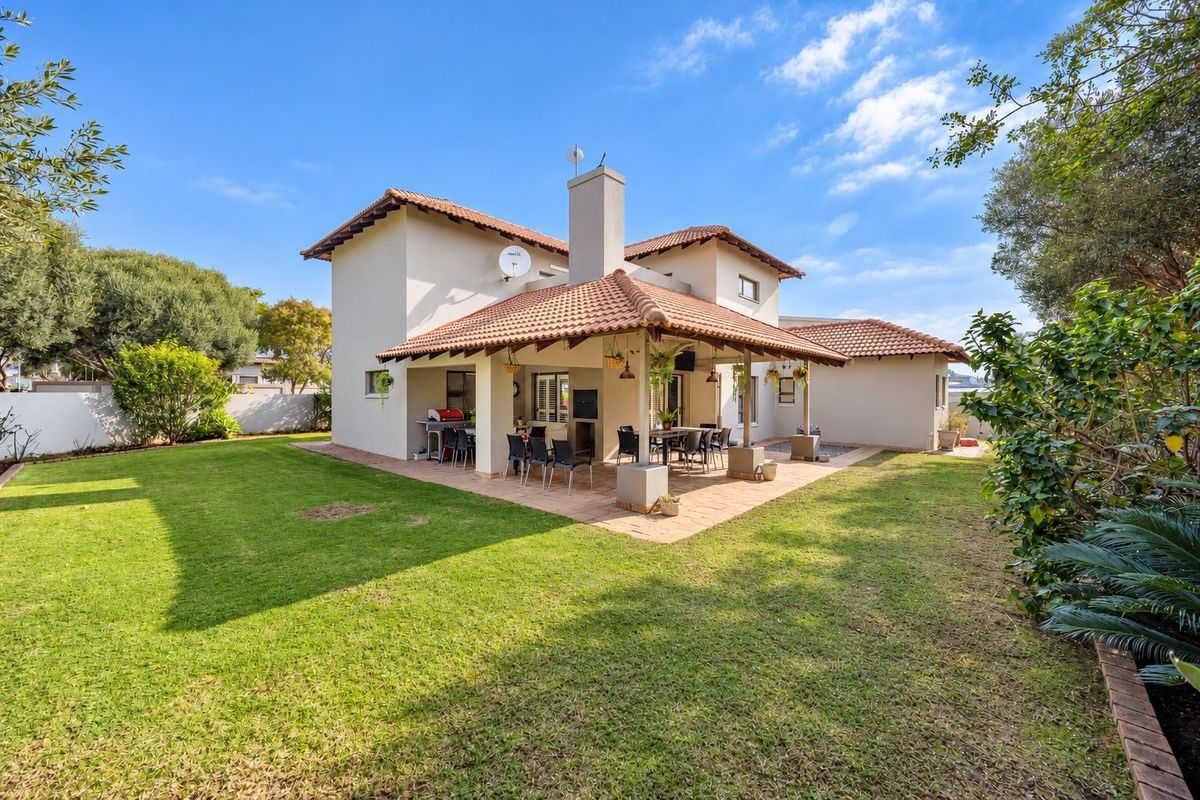Rear view of the house featuring a spacious covered patio with a built-in braai, overlooking a well-maintained garden and lawn area.
