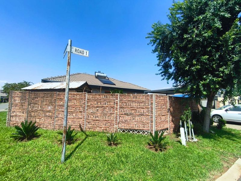 Street view of the property showing a brick boundary wall, tiled roof with solar water heater, and surrounding garden area.
