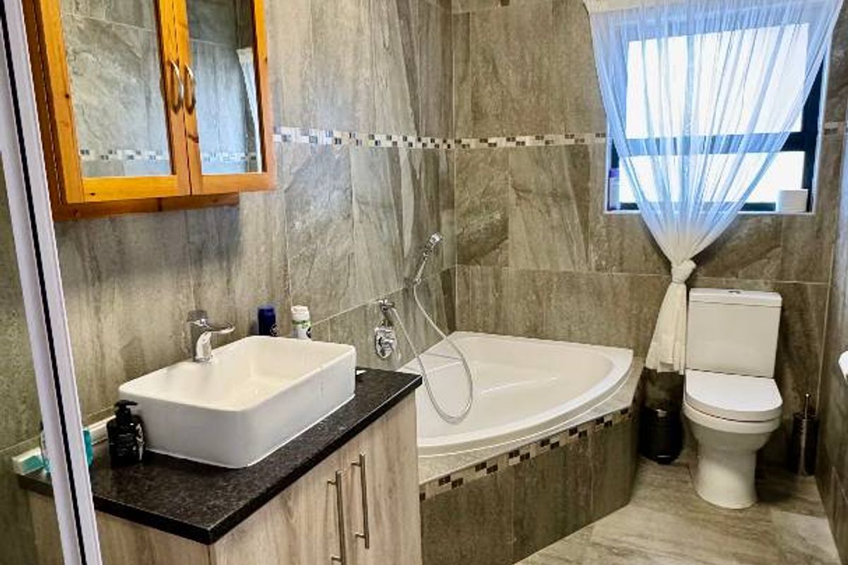 A modern bathroom featuring full-height stone-look wall tiles, a corner bathtub, a vanity with a vessel sink, and a separate shower enclosure.