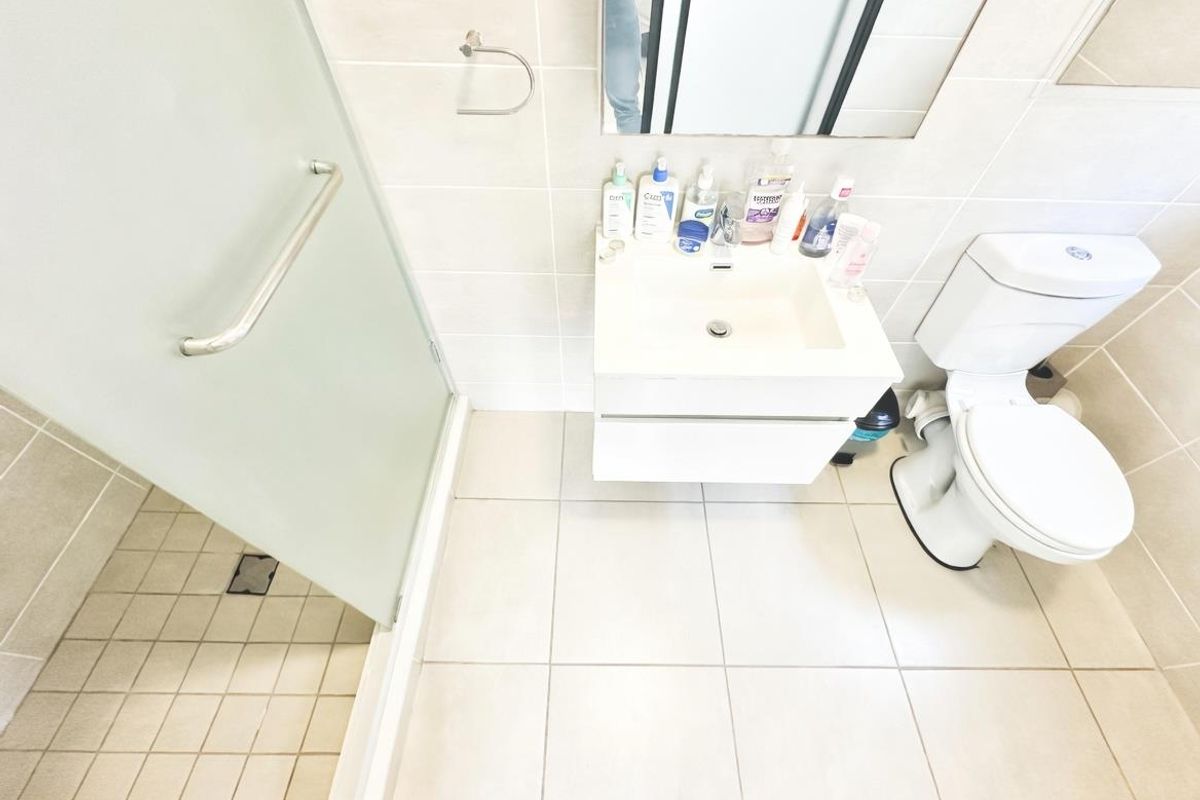 A clean, modern bathroom featuring a wall-mounted vanity, a glass-enclosed shower, and a standard toilet with neutral floor and wall tiling.