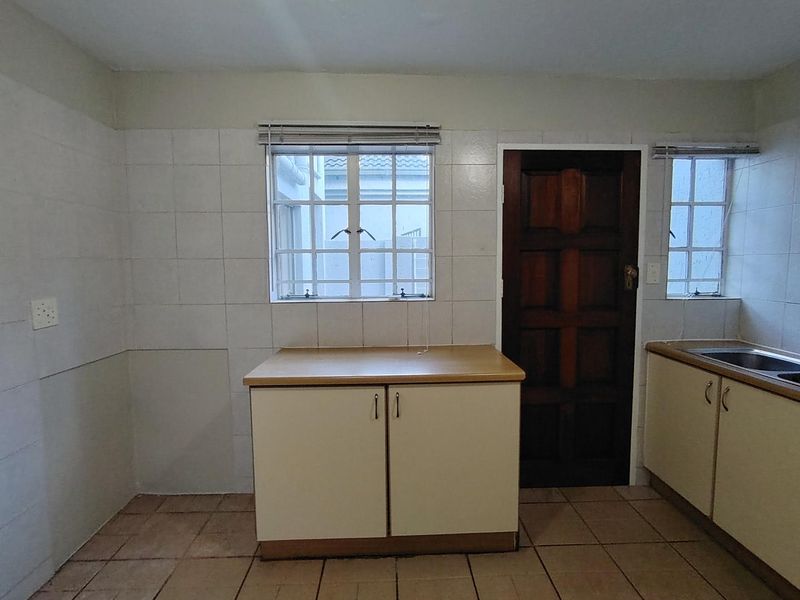 A functional kitchen area featuring tiled splashbacks, laminate countertops, built-in base cabinetry, and a stainless steel sink, ready for modernization.