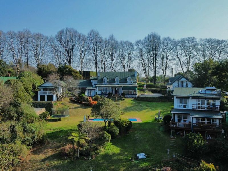 Aerial view of a sprawling property featuring multiple residential buildings, a swimming pool, expansive landscaped gardens, and mature trees.