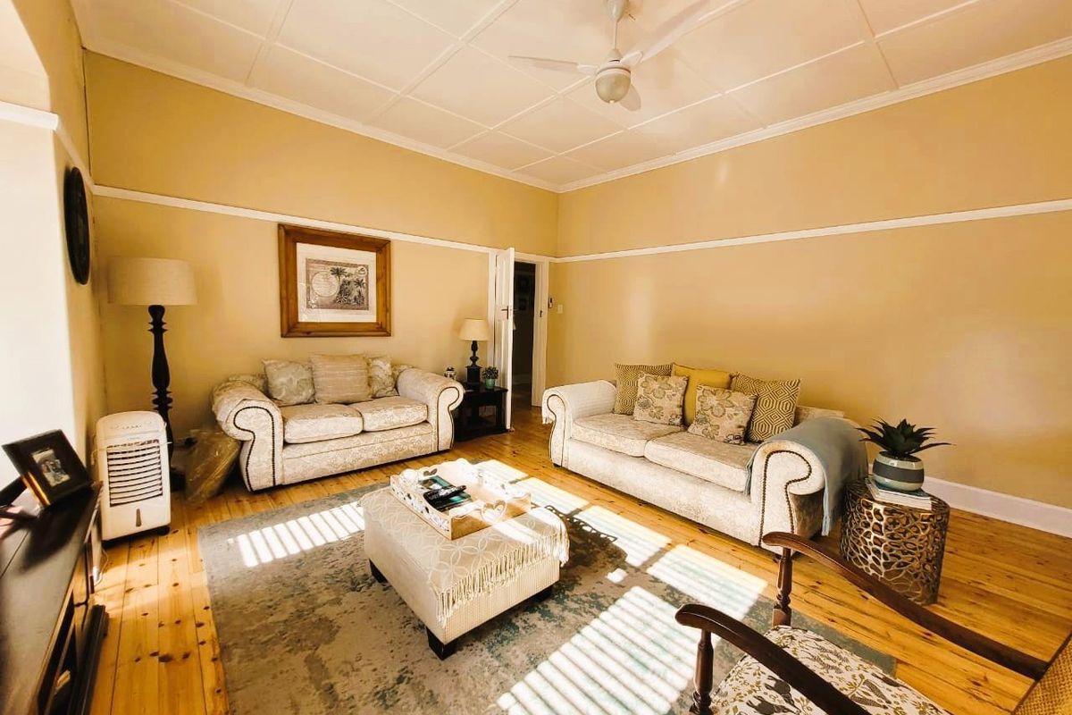A spacious living room featuring original timber flooring, high ceilings with a mounted fan, and classic picture rails.