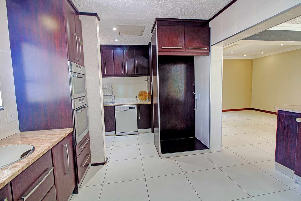 A functional kitchen featuring dark wood cabinetry, granite countertops, built-in oven, and tiled flooring, flowing into an adjacent open-plan living area.