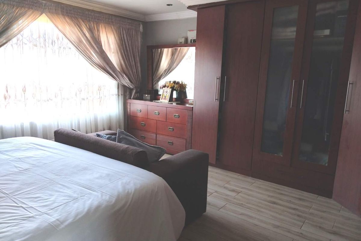 A bedroom featuring built-in wooden wardrobes, tiled flooring, and large windows with curtains, providing a functional and comfortable living space.