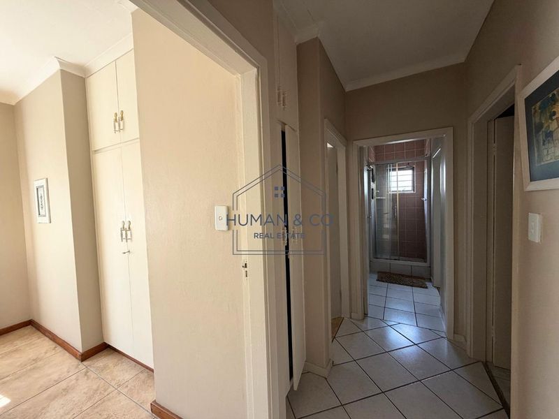 A functional hallway featuring built-in storage cupboards and tiled flooring, providing access to an adjacent bathroom with a shower enclosure.