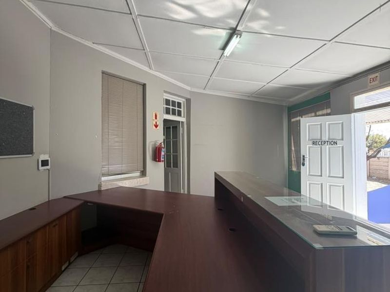 A functional office or reception area featuring a large built-in desk, tiled flooring, and a drop ceiling with integrated lighting.