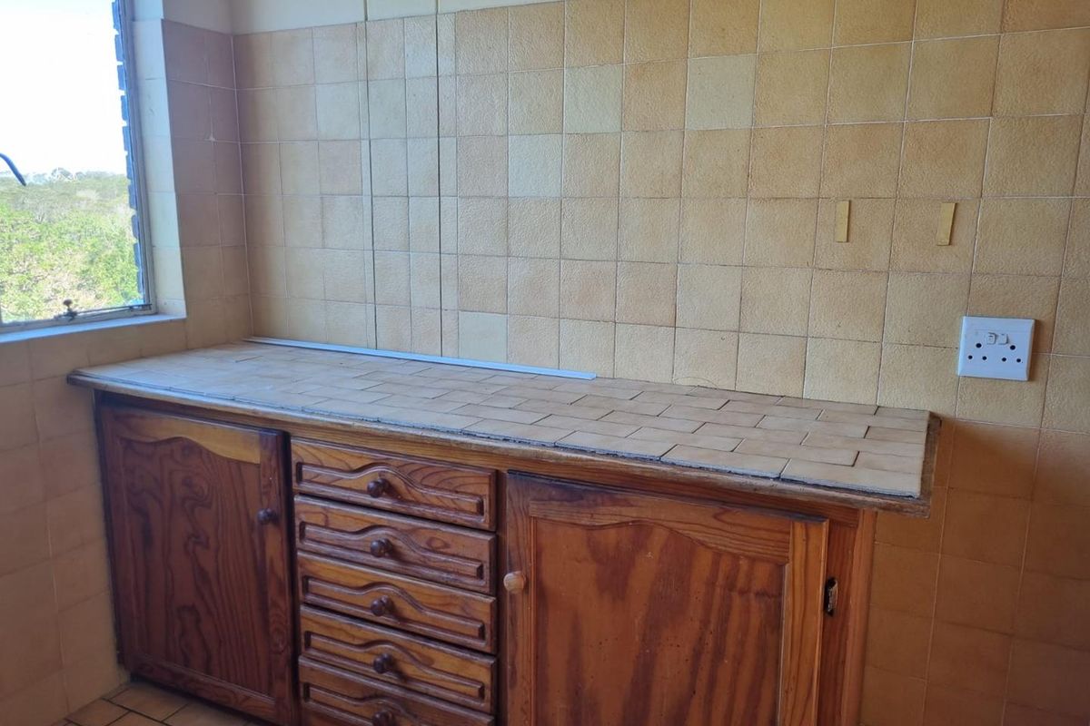A dated kitchen prep area featuring wooden cabinetry, tiled countertops, and full-height wall tiling, offering a functional space with potential for modernization.