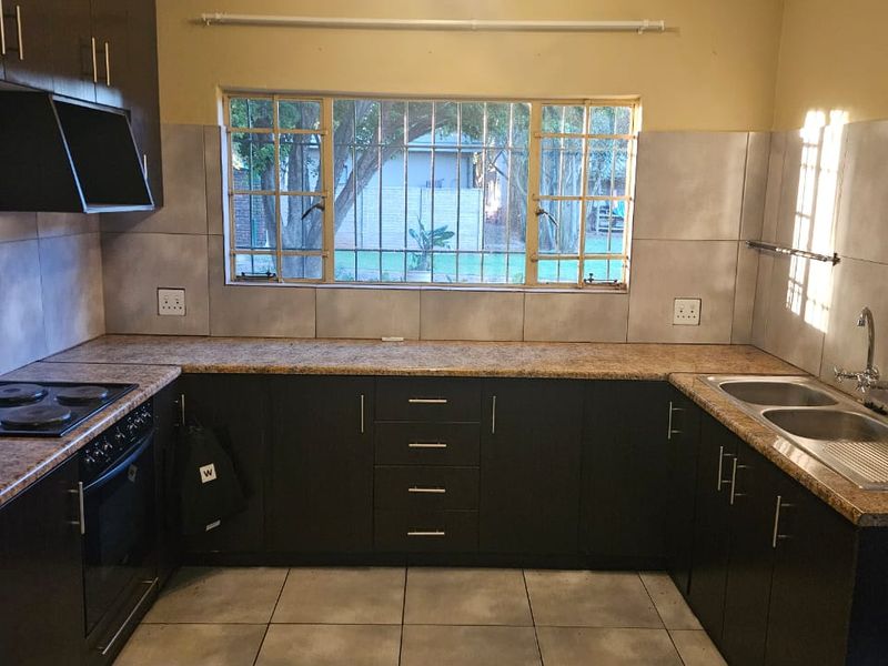 A functional U-shaped kitchen featuring dark cabinetry, laminate countertops, a double basin sink, and built-in oven with hob, overlooking the garden.
